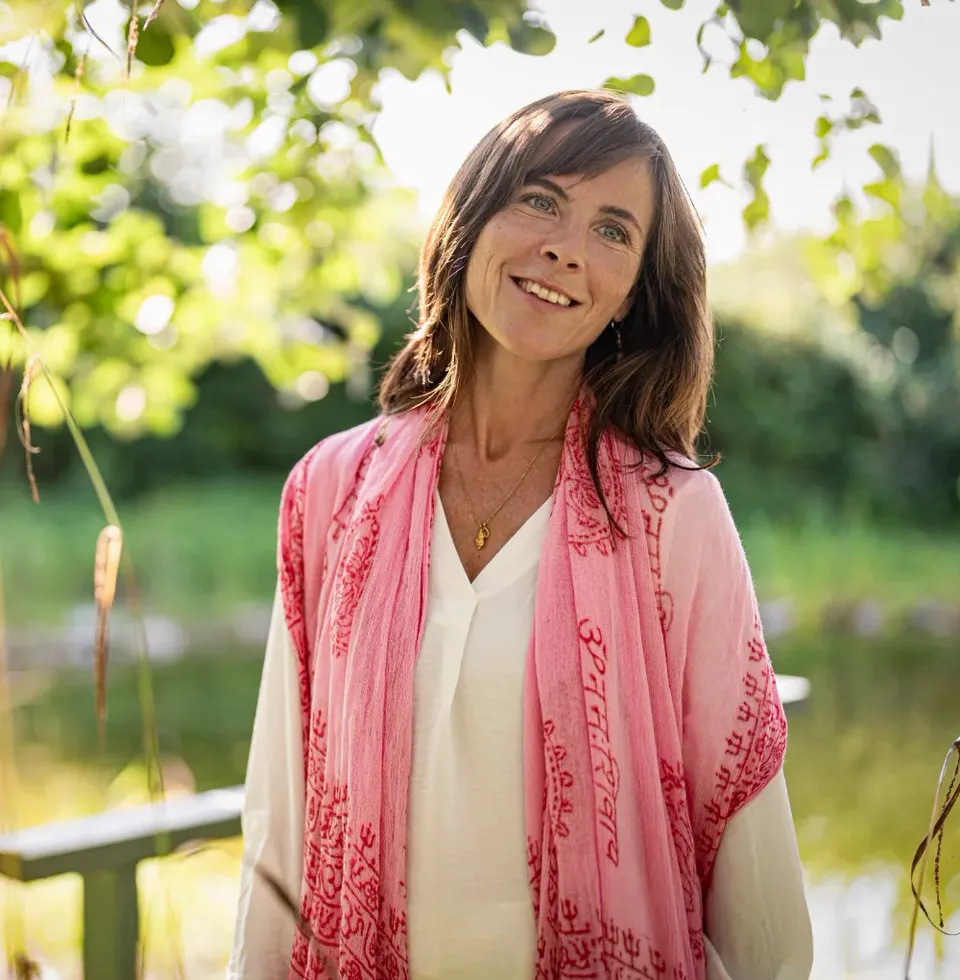 Diana Ernst im Freien, mit einem rosafarbenen Schal, am Wasser stehend